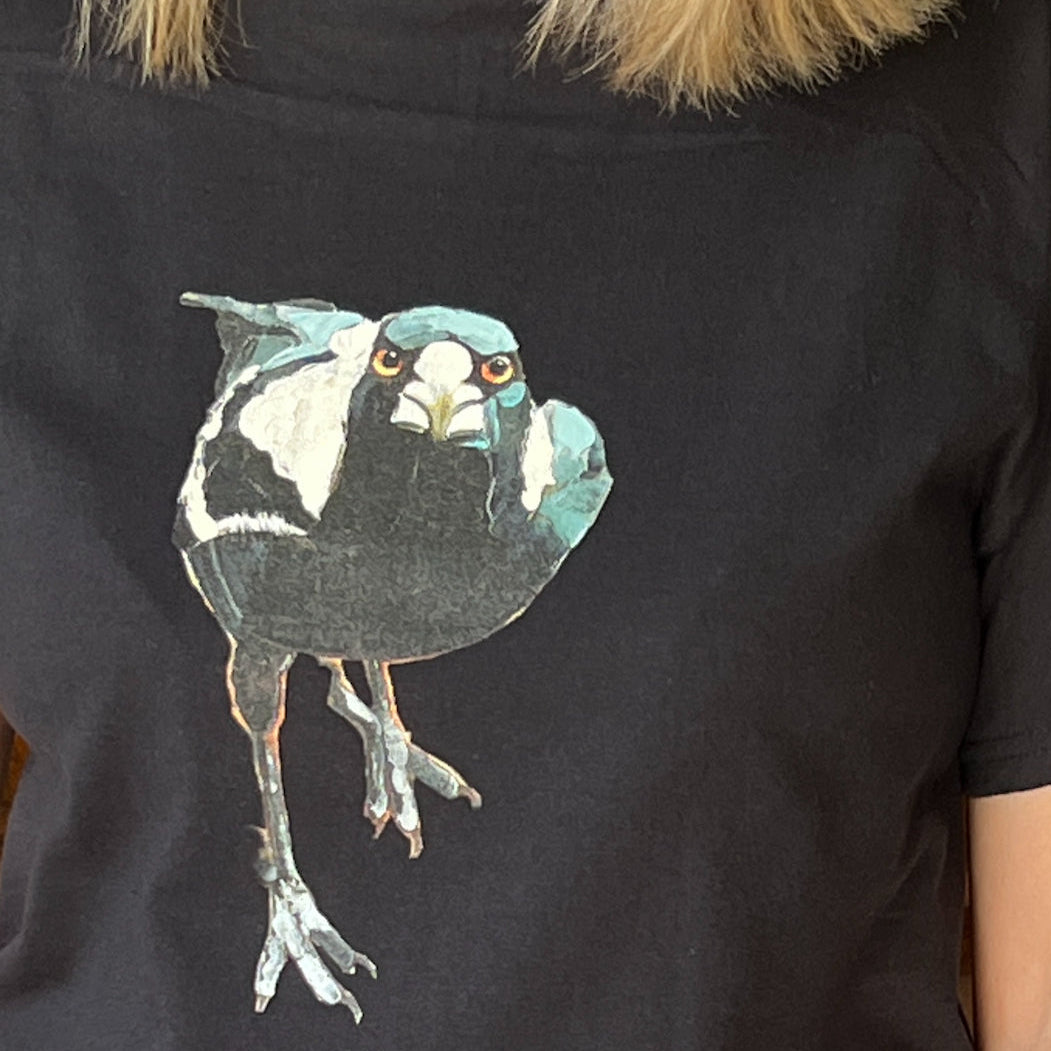 Black t-shirt with a colorful bird fierce magpie graphic on a person wearing a fur-lined hood.