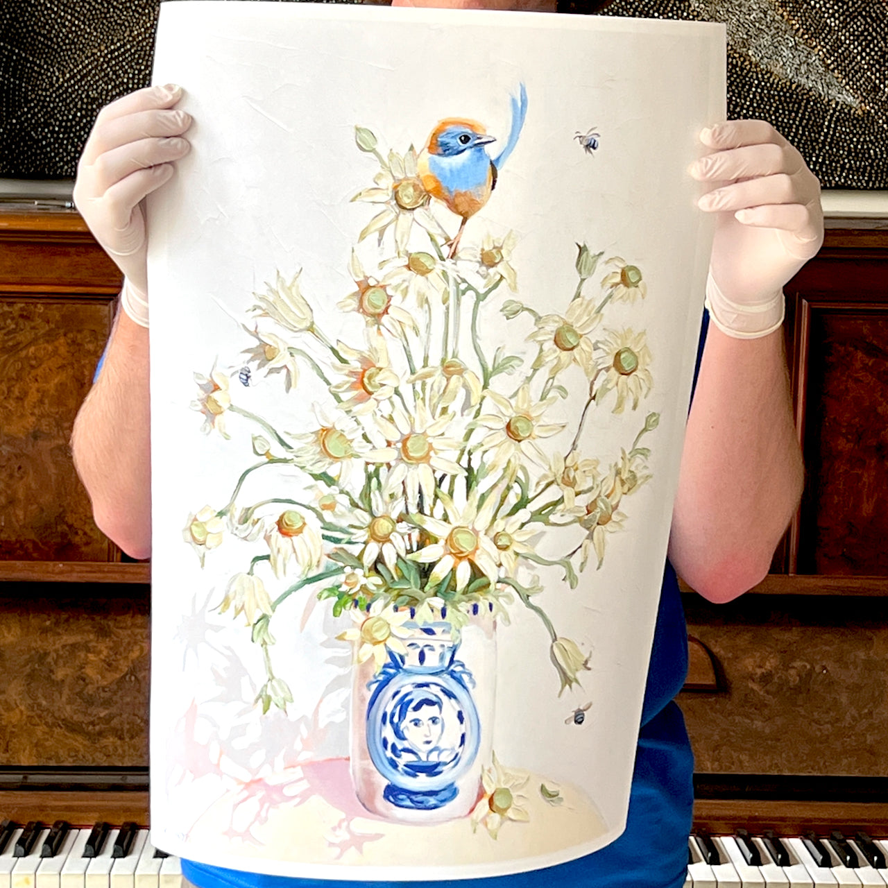 Person holding a painting of flowers and a bird on a white background giclee print by artist Kirsty McIntyre blue wren with flannel flowers