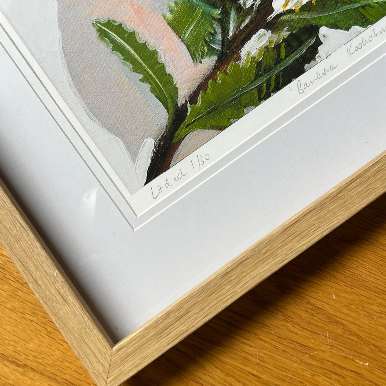 Framed botanical illustration with a signature on a wooden surface