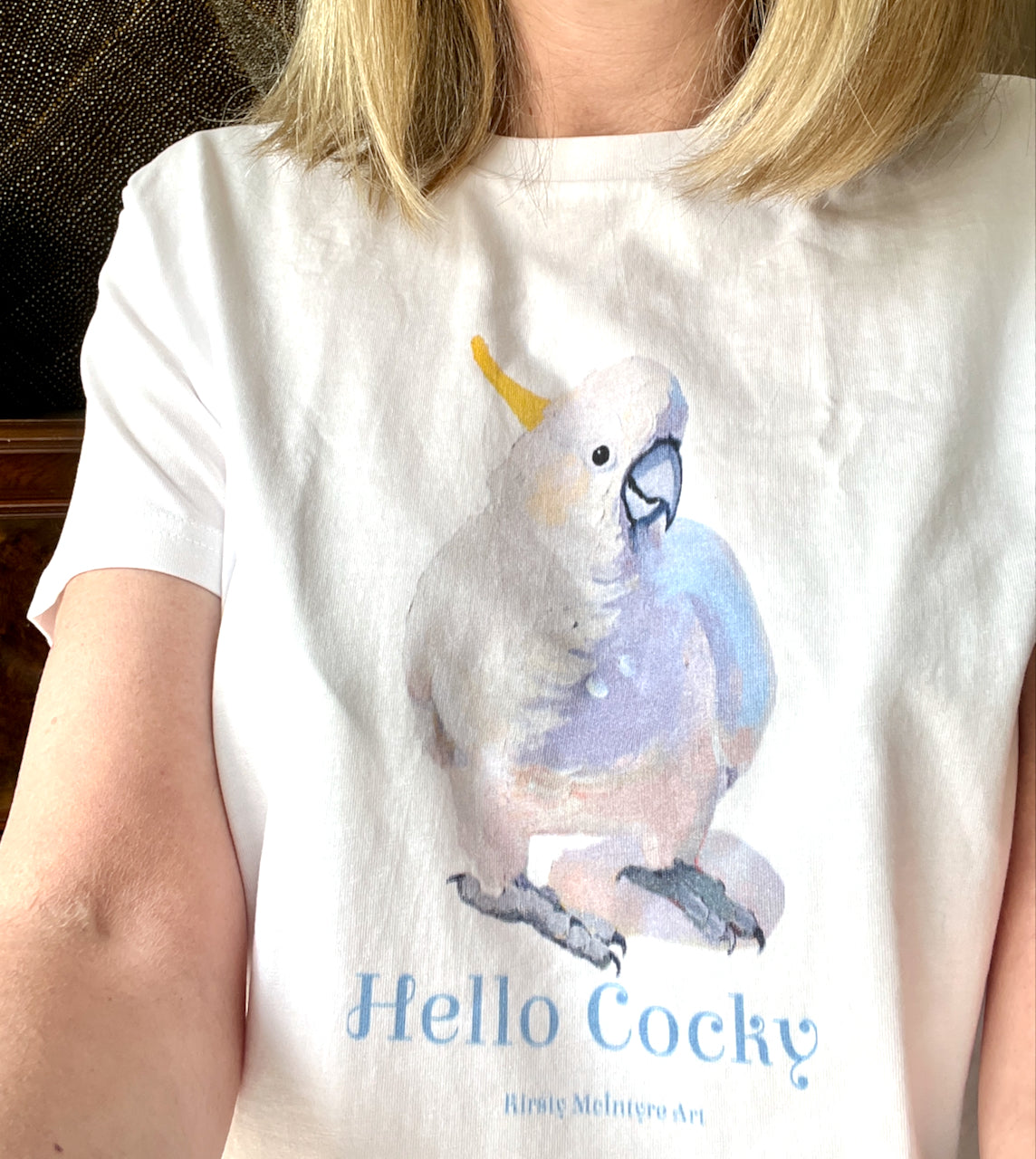 Person wearing a womens white t-shirt with an original cockatoo parrot design  by Kirsty McIntyre Art and 'Hello Cocky' text. 