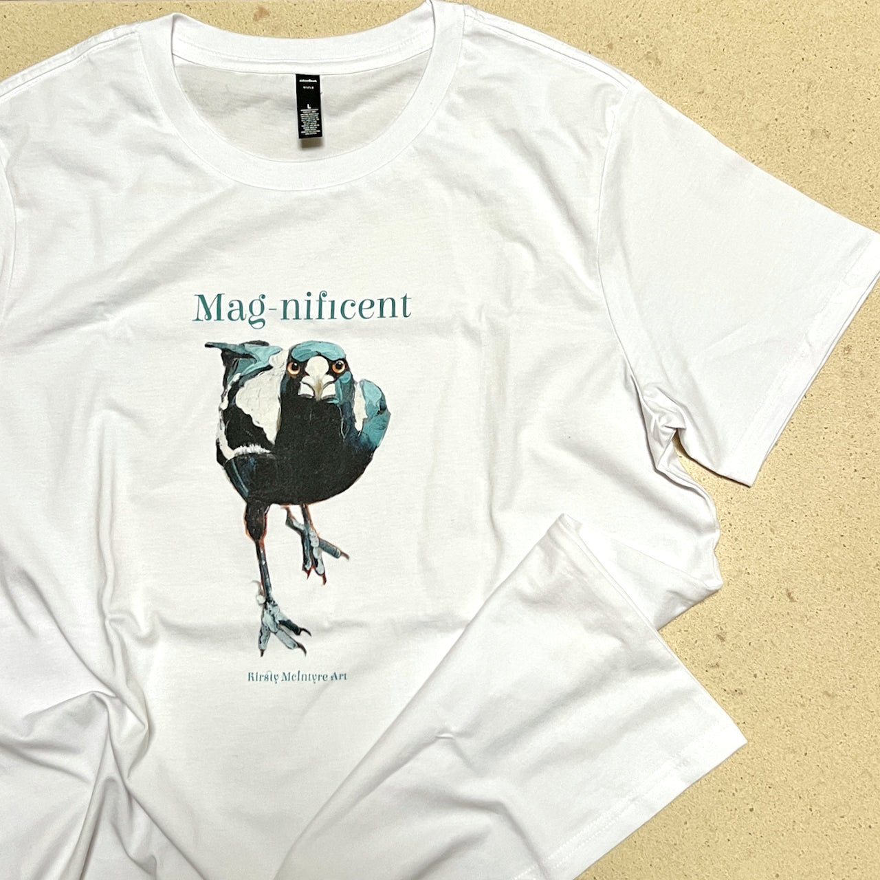 White t-shirt with a bird graphic and 'Mag-nificent' text on a beige background original design by popular best australian bird artist, Kirsty McIntyre