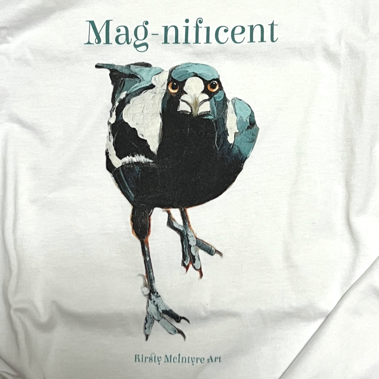 White t-shirt with an australian native magpie bird original illustration by artist Kirsty McIntyre and the word 'Mag-nificent' above it, on a white background.