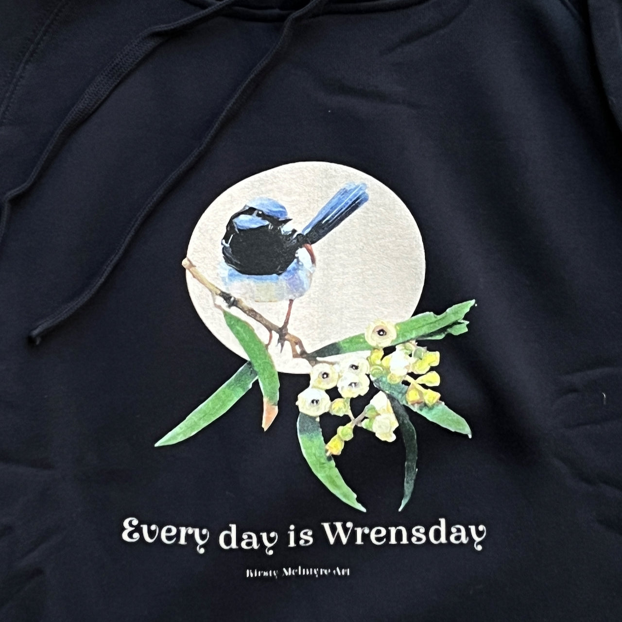 Navy blue hoodie with a superb blue wren bird design and text 'Every day is Wrensday' on a branch with leaves and flowers. original desing by artist australian Kirsty McIntyre