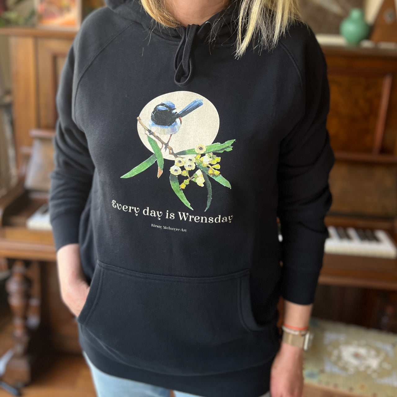 person wearing a navy blue hoodie with a superb blue wren bird design and text 'Every day is Wrensday' on a branch with leaves and flowers. original design by artist australian Kirsty McIntyre