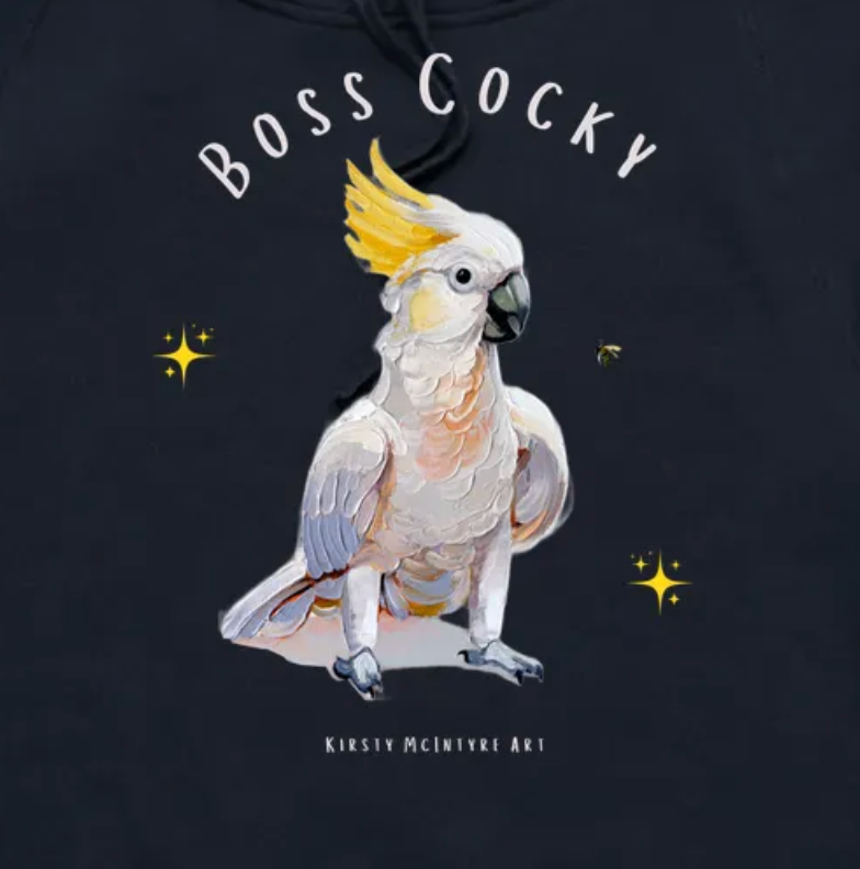 Black hoodie with a cockatoo illustration and 'Boss Cocky' text on a dark background. Close up of a a navy blue t-shirt with a parrot graphic and text 'Boss Cocky' on a white background. Original cockatoo tshirt design by artist, Kirsty McIntyre, australian.