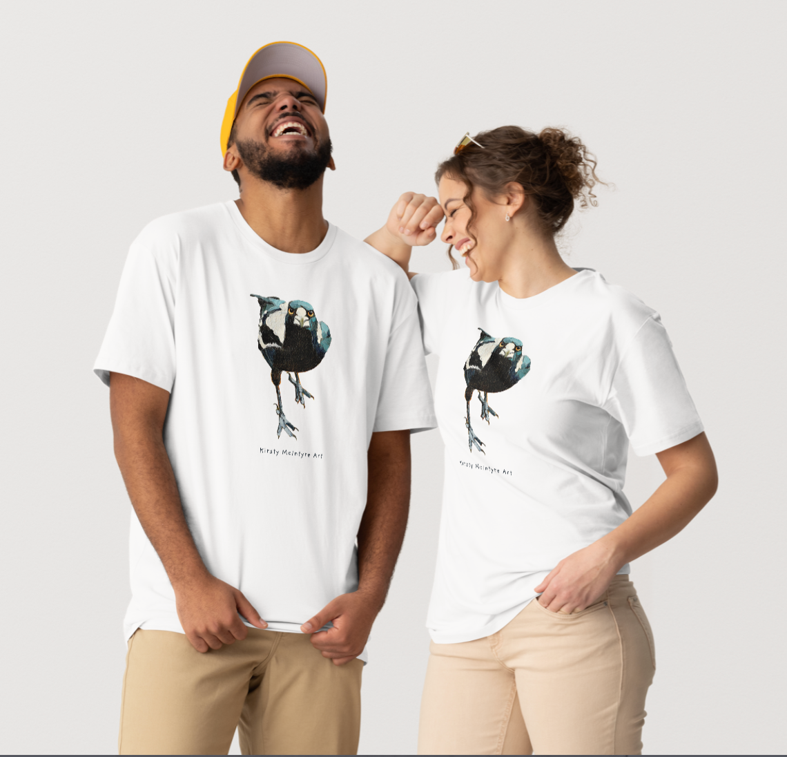 Two people wearing white t-shirts with a graphic design on a light gray background  featuring an original staring, fierce magpie graphic design by Kirsty McIntyre, australian bird lover and artist