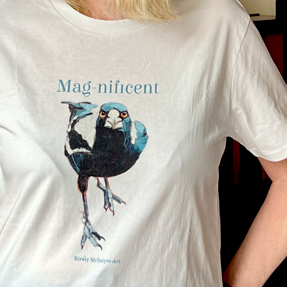 White t-shirt with a blue and black australian magpie bird graphic original design by australian artist Kirsty McIntyre and the word 'Magnificent' on a person wearing it.
